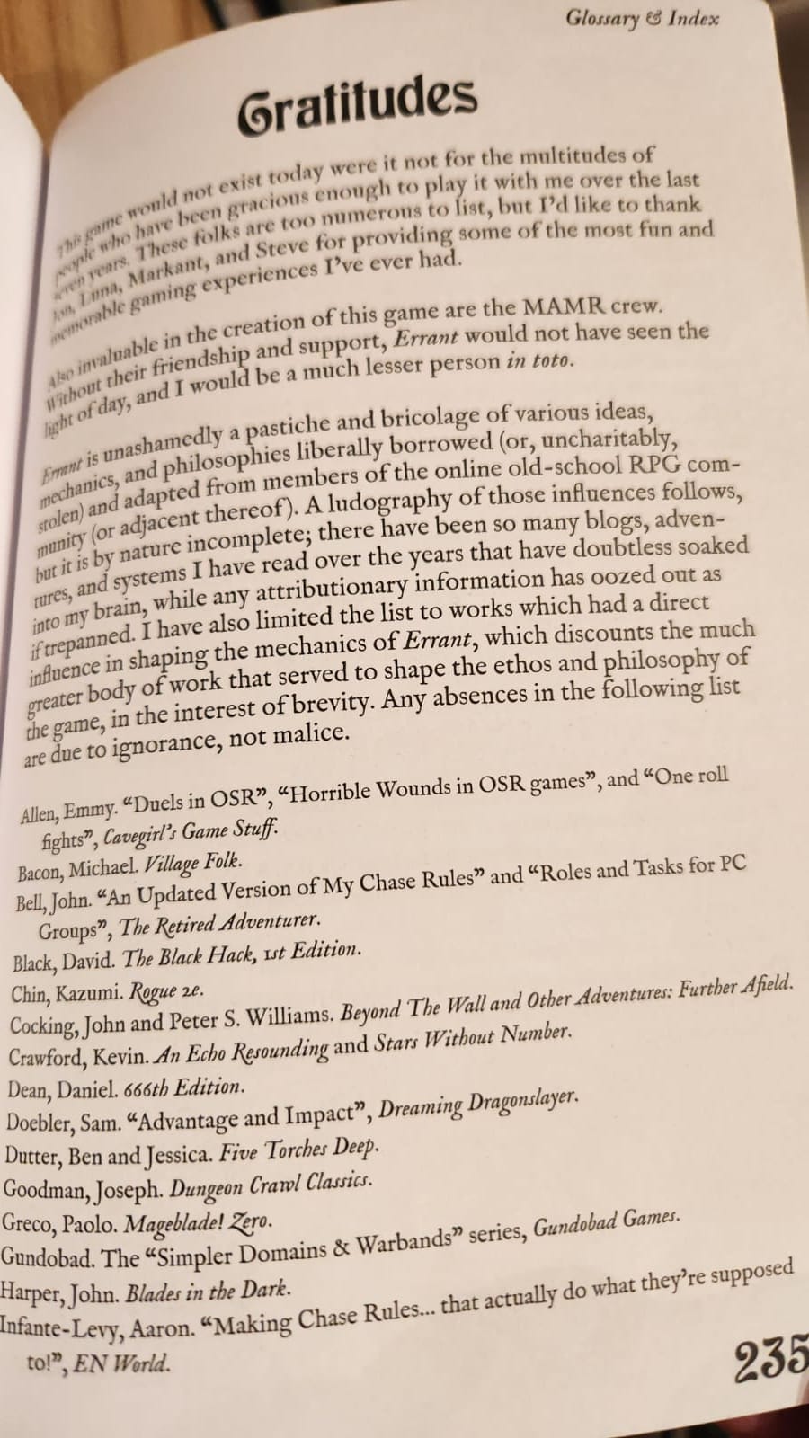 La foto de una pàgina de Errant, con este texto: "Gratitudes This game would not exist today were it not for the multitudes of people who have been gracious enough to play it with me over the last seven years. These folks are too numerous to list, but I’d like to thank Robin, Markant, and Steve for providing some of the most fun and memorable gaming experiences I’ve ever had. Also invaluable in the creation of this game are the MAMR crew. Without their friendship and support, Errant would not have seen the light of day, and I would be a much lesser person in toto. Errant is unashamedly a pastiche and bricolage of various ideas, mechanics, and philosophies liberally borrowed (or, uncharitably, stolen) and adapted from members of the online old-school RPG com- munity (or adjacent thereof). A ludography of those influences follows, but it is by nature incomplete; there have been so many blogs, adven- tures, and systems I have read over the years that have doubtless soaked into my brain, while any attributionary information has oozed out as firepanned. I have also limited the list to works which had a direct influence in shaping the mechanics of Errant, which discounts the much greater body of work that served to shape the ethos and philosophy of the game, in the interest of brevity. Any absences in the following list are due to ignorance, not malice."